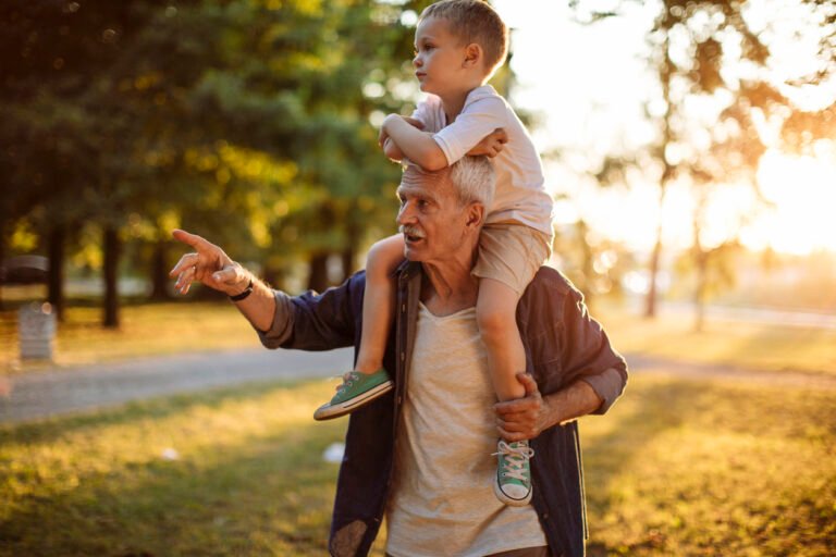 Grandfather carrying his grandchild on shoulders outside in the park